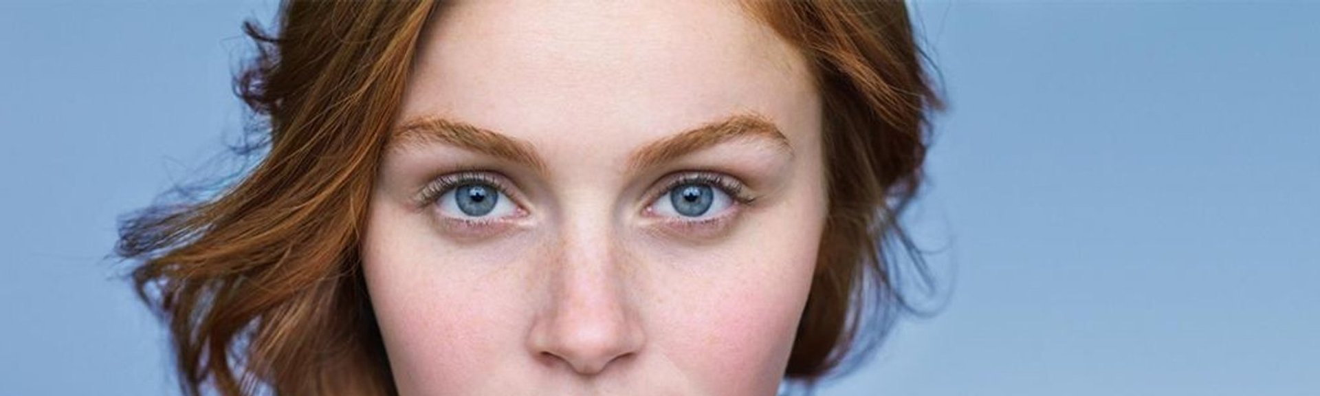 En rödhårig kvinna med blå ögon och synlig rodnad på kinderna, typiskt för rosacea-benägen hud