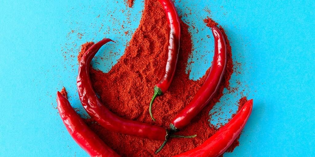 Hela röda chilifrukter och ett fint rött chilipulver spritt mot en livfull turkos bakgrund